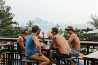 un grupo de hombres sentados en una mesa frente al océano en Balcony Party Hostel - 18-40, en Ao Nang Beach