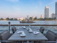 a table with chairs and a boat on the water at Chatrium Hotel Riverside Bangkok in Bangkok