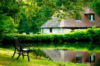 a park bench sitting in the grass next to a pond at Au Moulin de La Gorce in La Roche-lʼAbeille