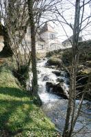 a stream of water with a house in the background at Au Moulin de La Gorce in La Roche-lʼAbeille