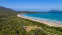 a house on a hill next to a beach at Cloudy Bay Cabin in South Bruny