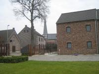 a brick building with a church in the background at Hotel Oude Eycke in Maaseik
