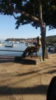 a statue of a man sitting on a bench next to the water at Pousada Portico de Buzios in Armacao dos Buzios