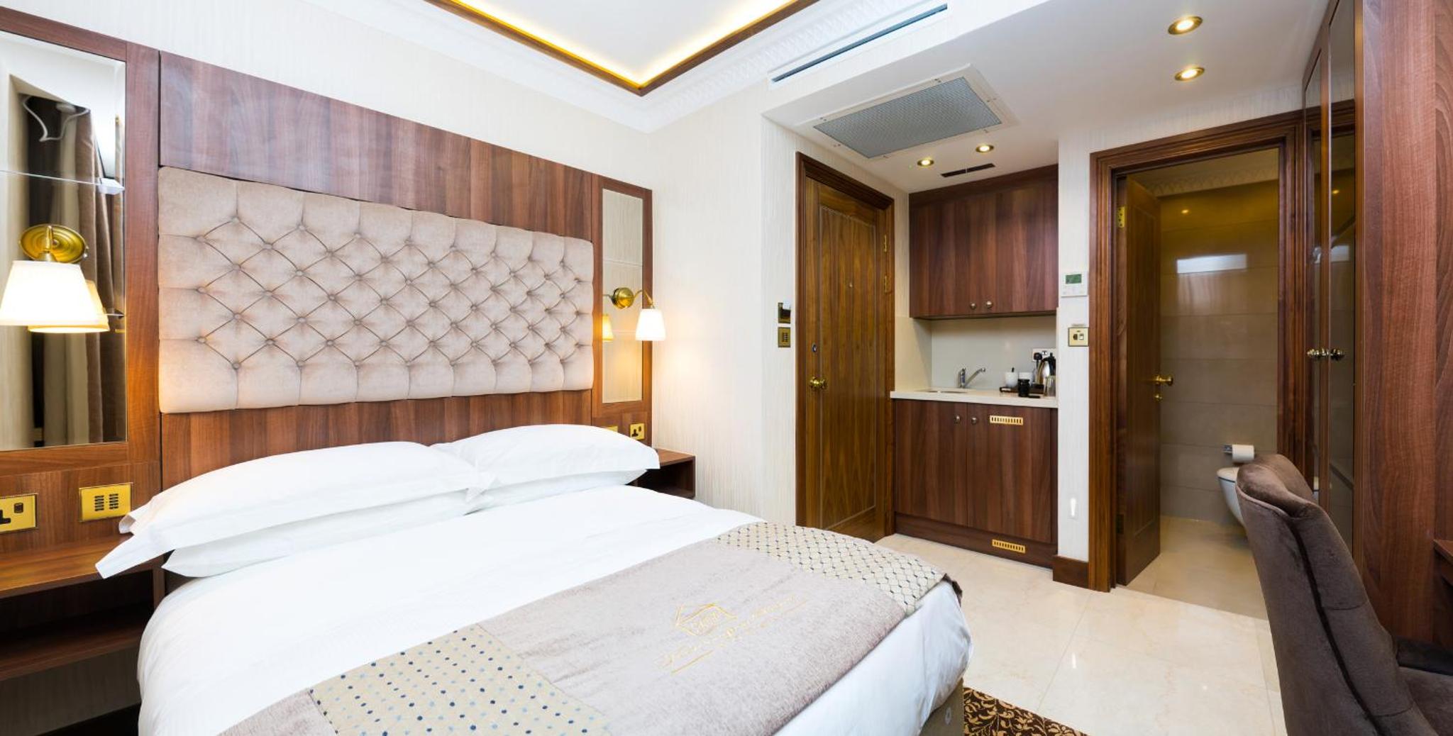 a bedroom with a white bed and a wooden headboard at Kensington Prime Hotel in London +39 photos