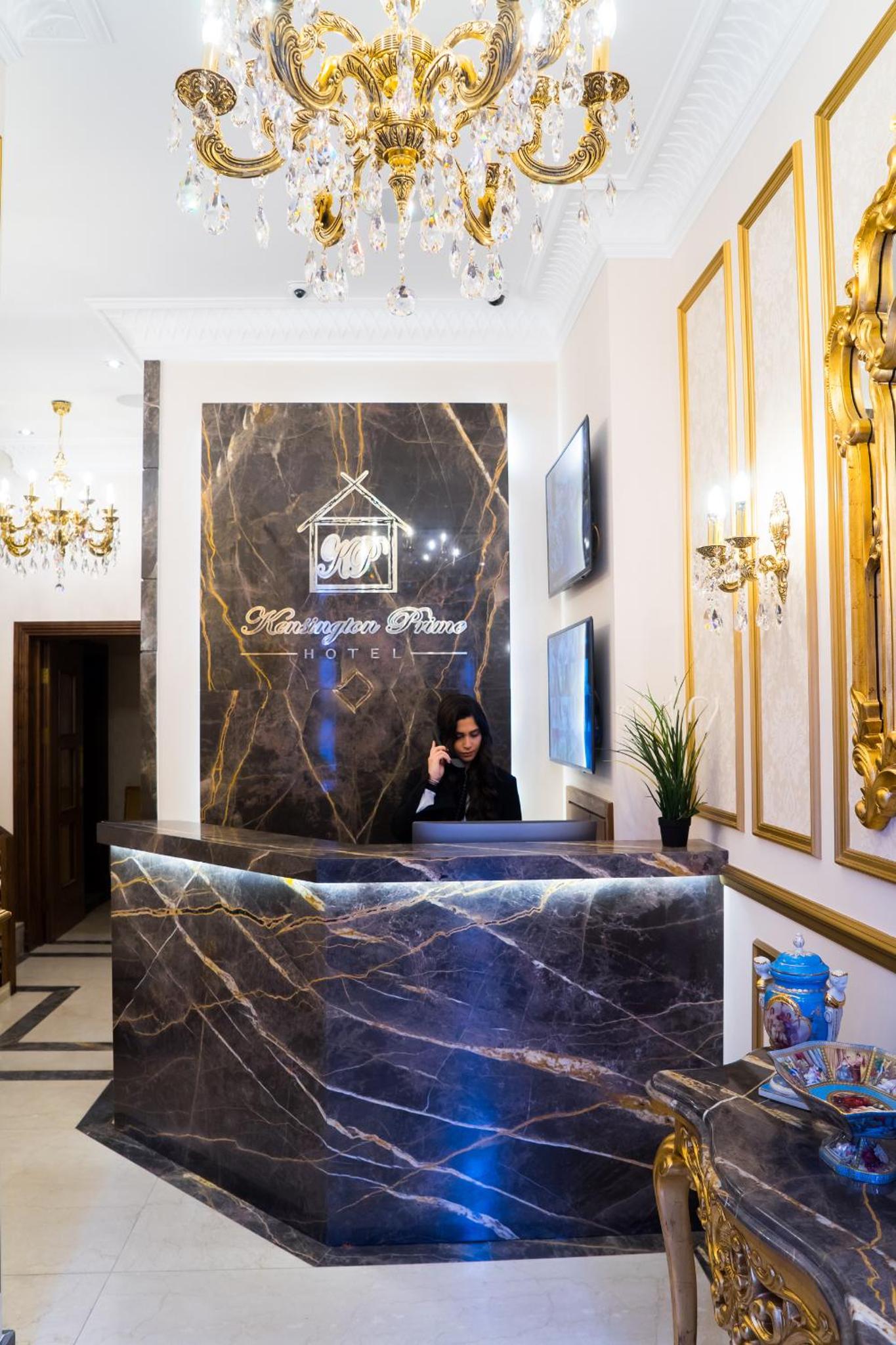 a woman standing behind a counter in a room with a chandelier at Kensington Prime Hotel in London