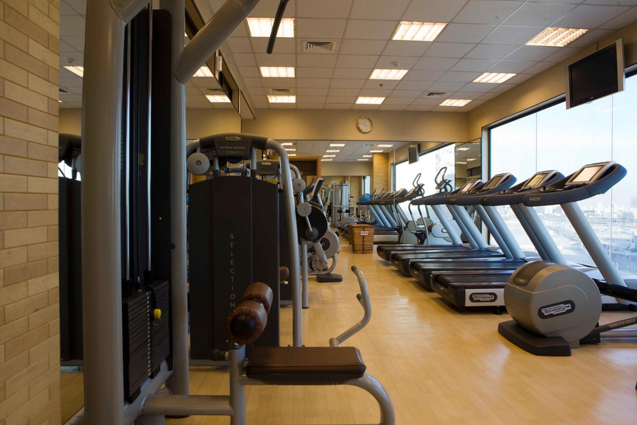 a gym with rows of treadmills and elliptical machines at City Center Hotel in Manama