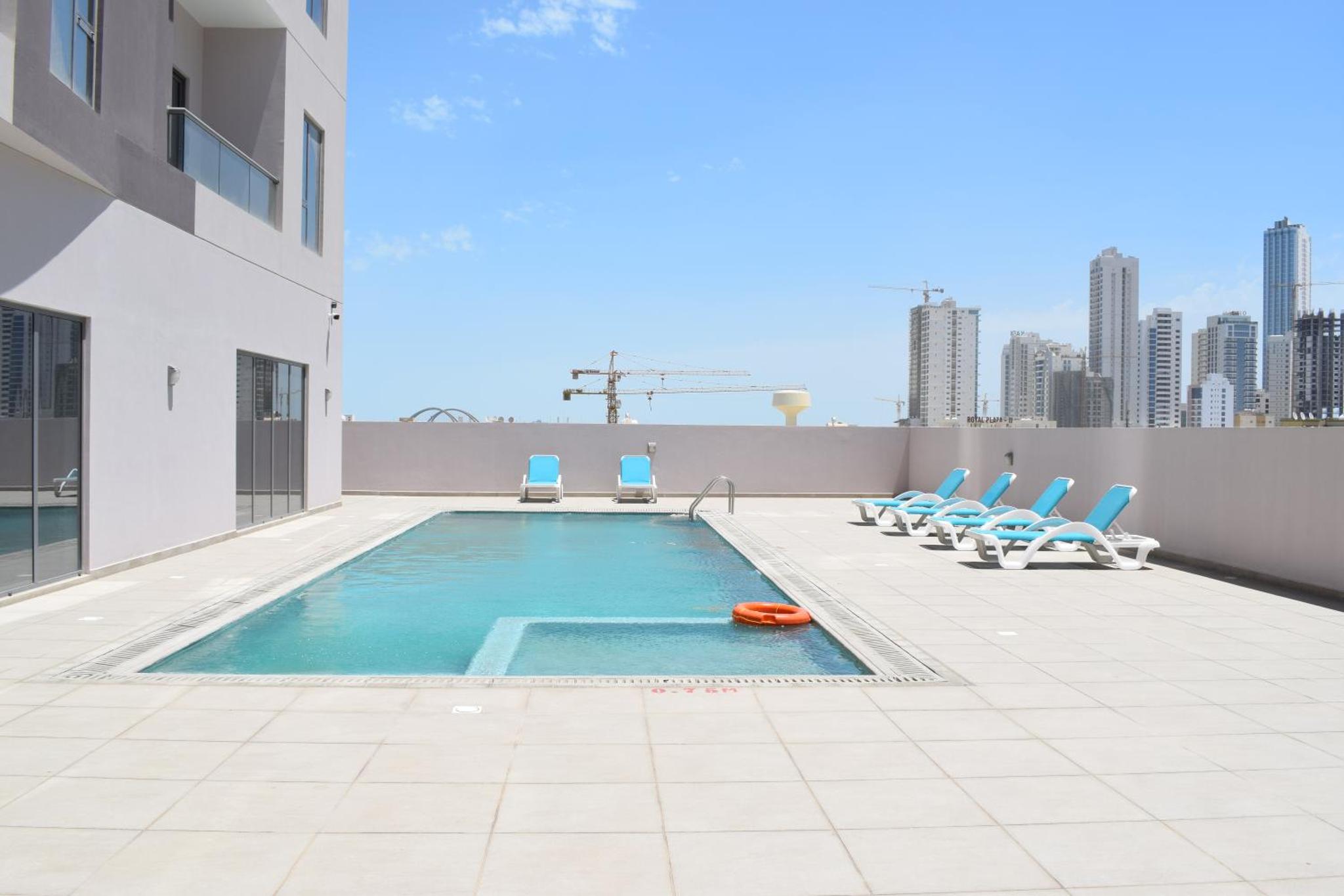 a swimming pool on the roof of a building with chairs at The Spot Residence in Juffair