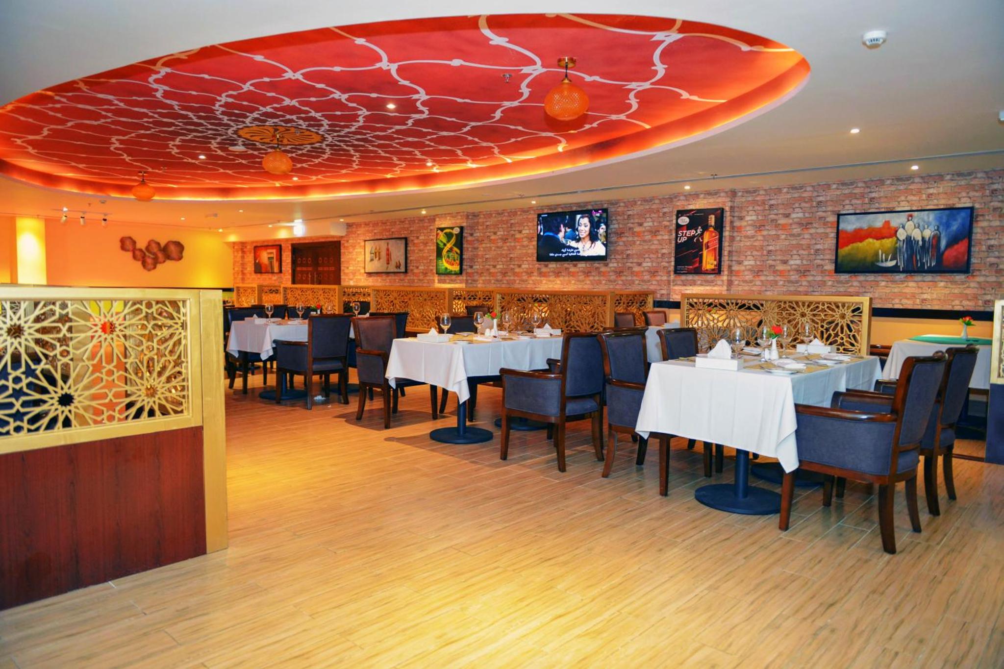 a restaurant with white tables and chairs and a red ceiling at Meshal Hotel in Manama