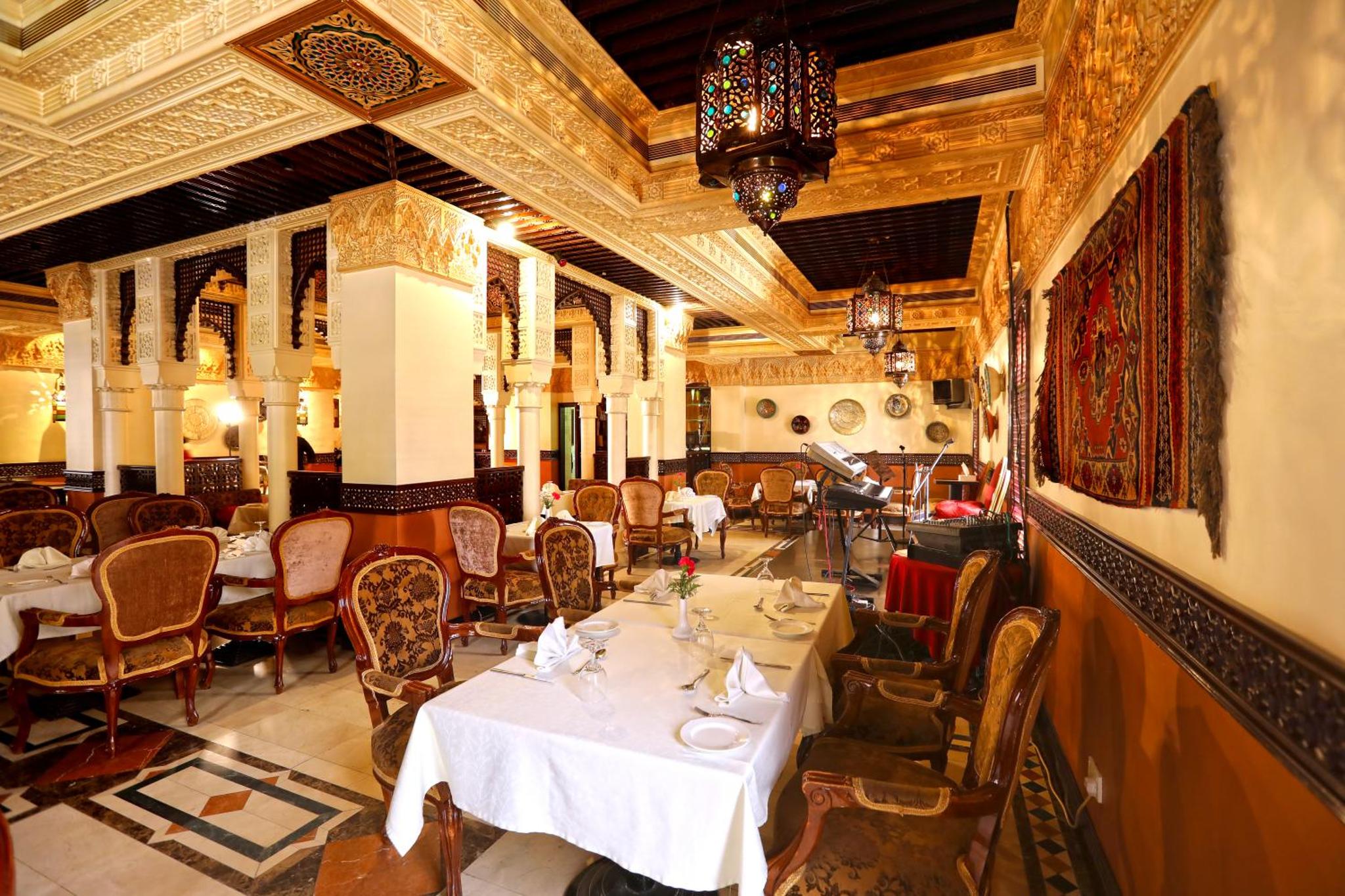 a restaurant with tables and chairs and a chandelier at Delmon International Hotel in Manama