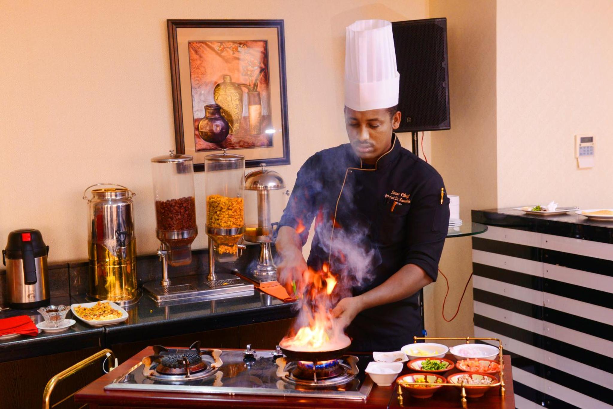 a man cooking food on a stove in a kitchen at Juffair Gate Hotel in Manama +70 photos