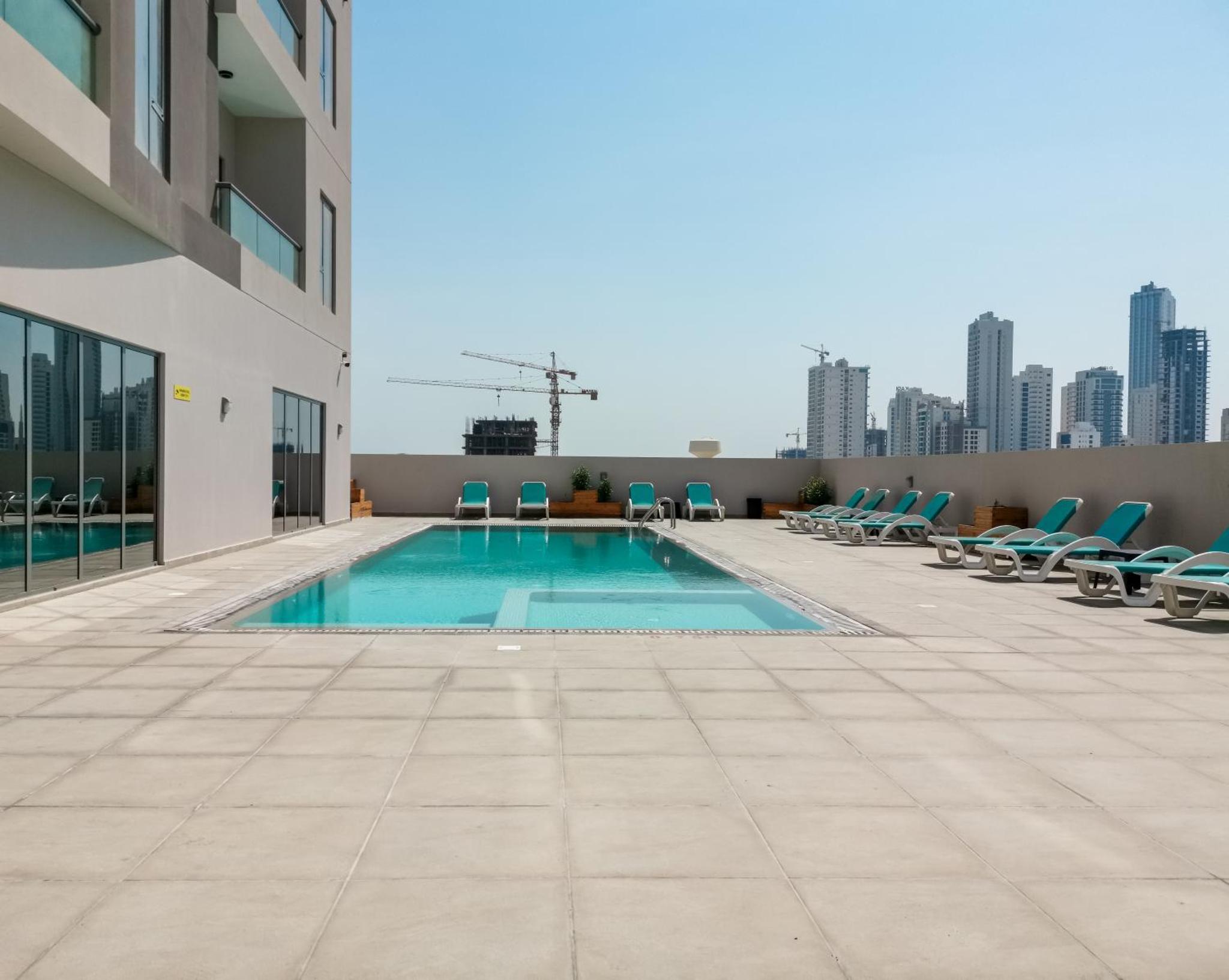 a swimming pool on the roof of a building with chairs at The Spot Residence in Juffair