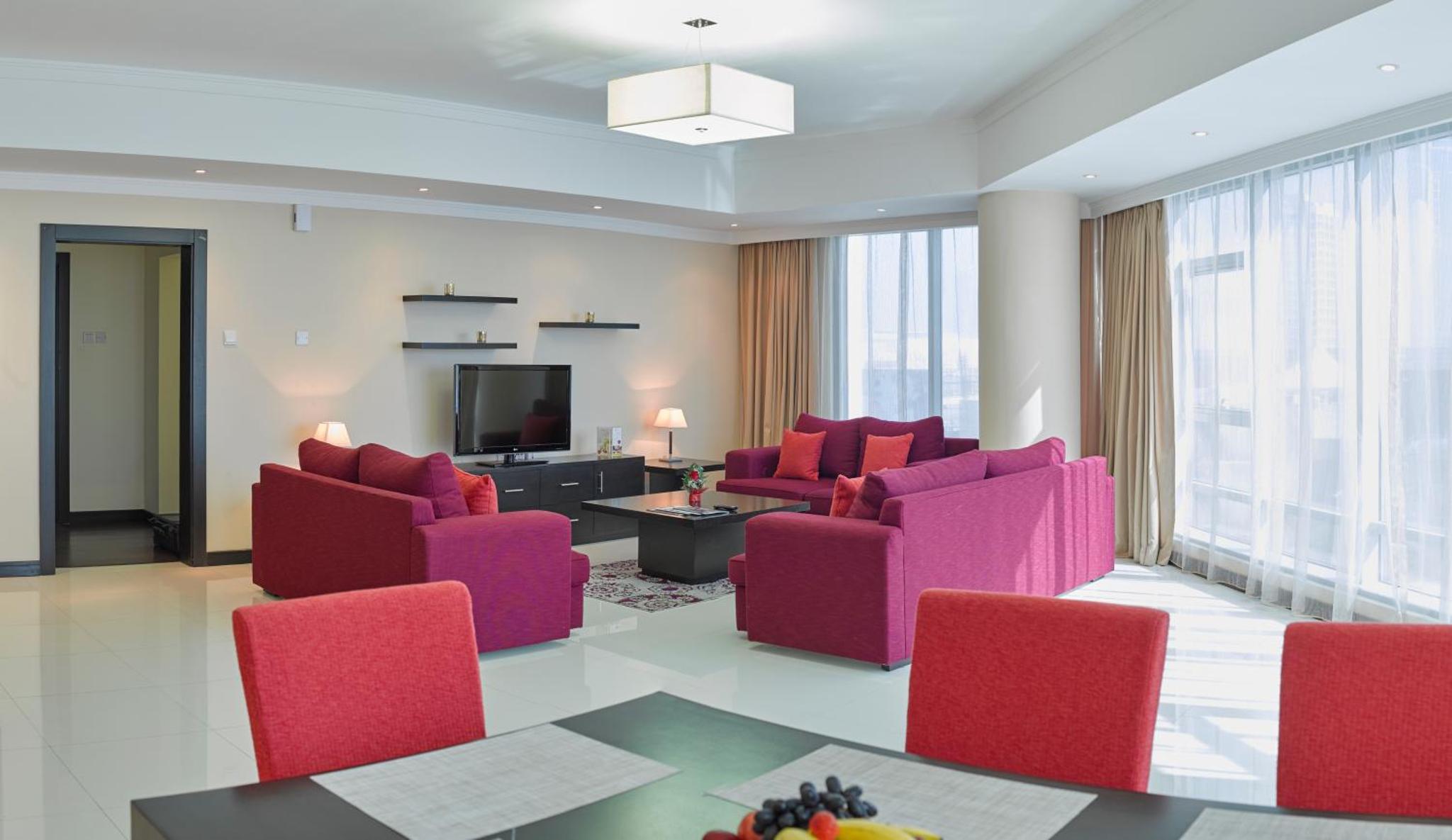 a living room with red chairs and a television at Tulip Hotel & Suites in Manama
