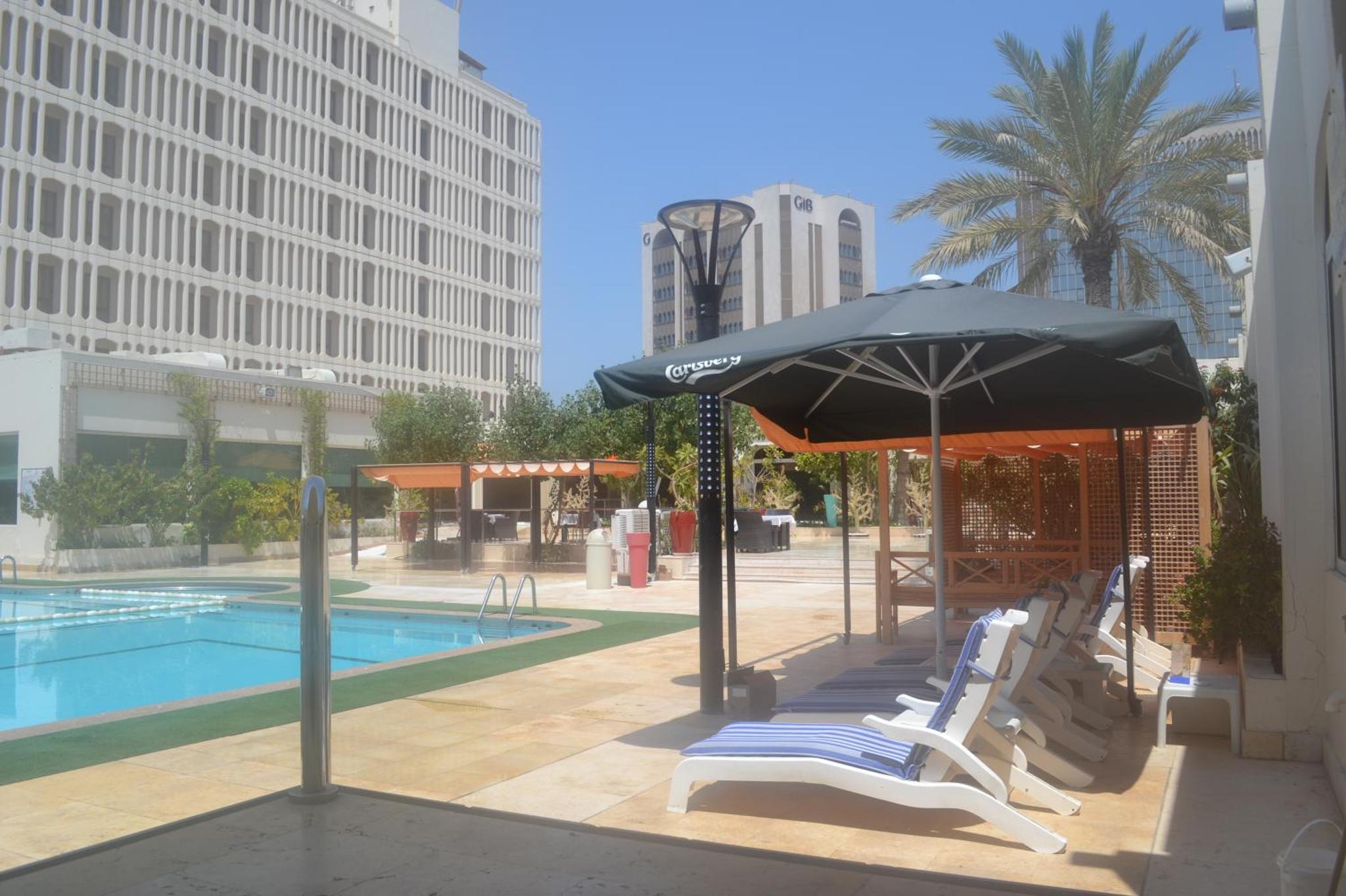 a group of chairs and an umbrella next to a pool at Golden Tulip Bahrain in Manama
