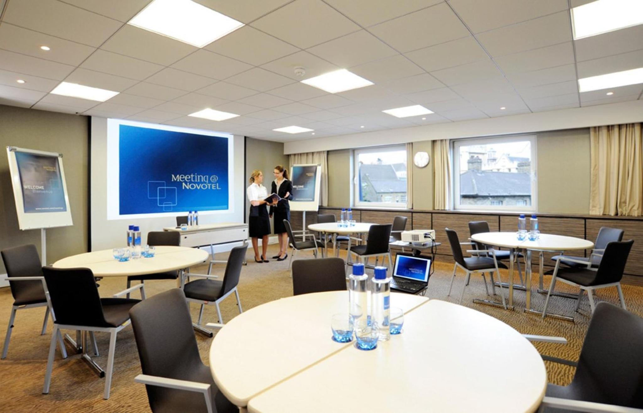 a meeting room with tables and chairs and two people at Novotel London Waterloo in London