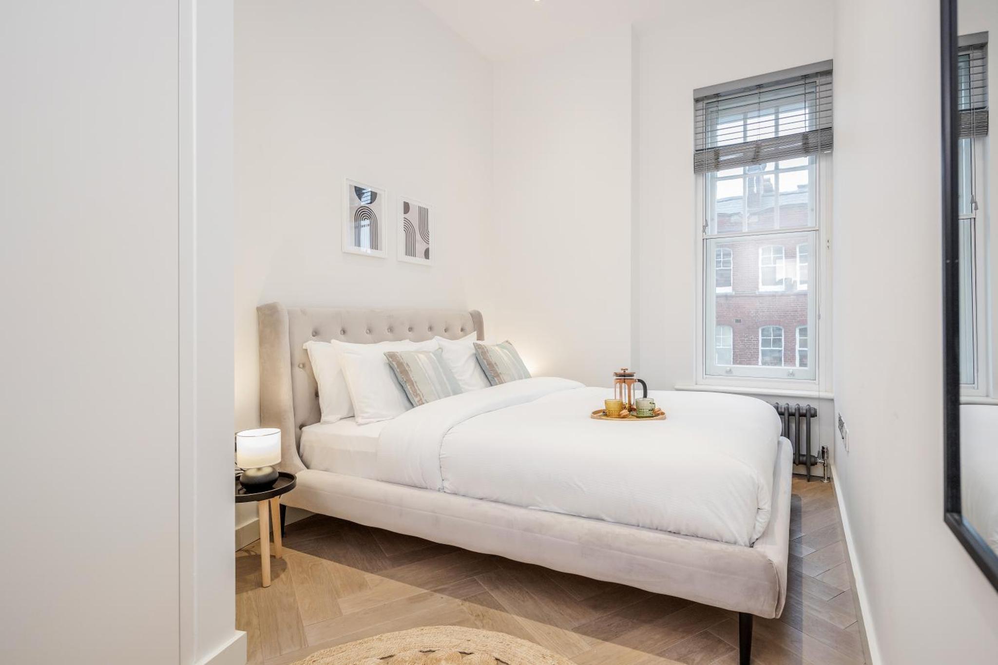a white bedroom with a bed and a window at Stay Kula London - Fitzrovia Newman St in London