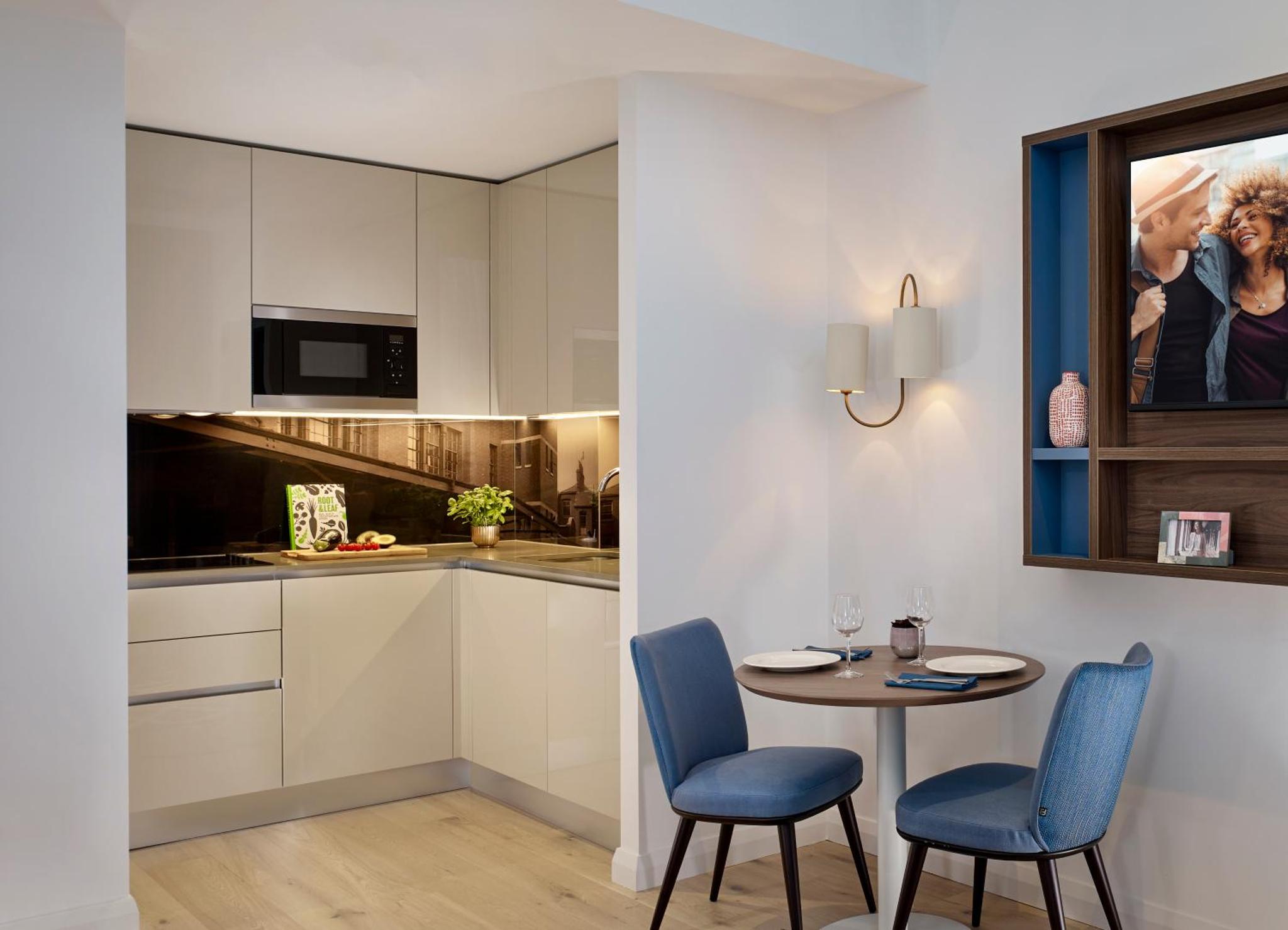 a kitchen with a table and two blue chairs at Citadines Islington London in London
