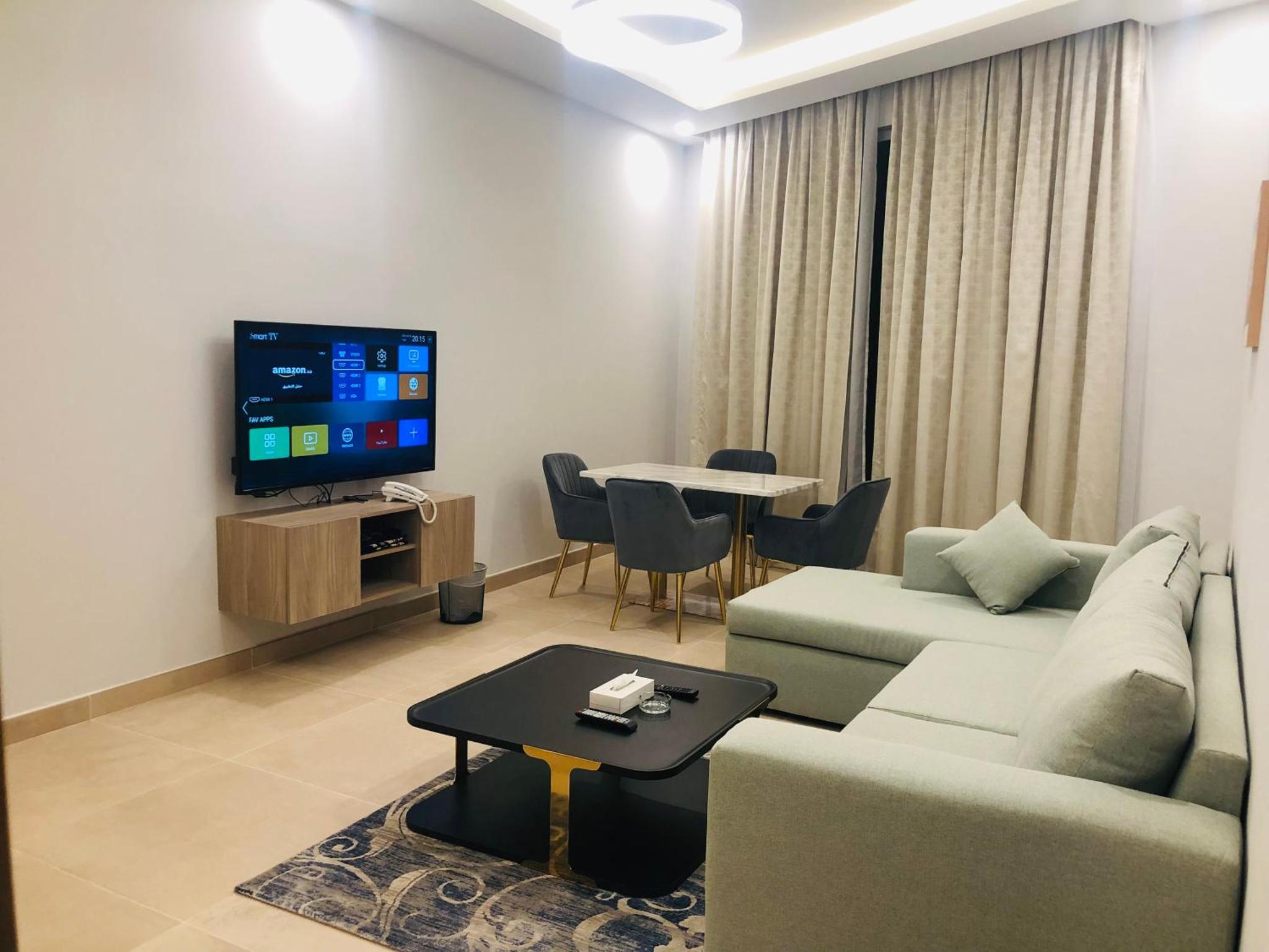 a living room with a couch and a tv and a table at JOOD RESIDENCE in Seef