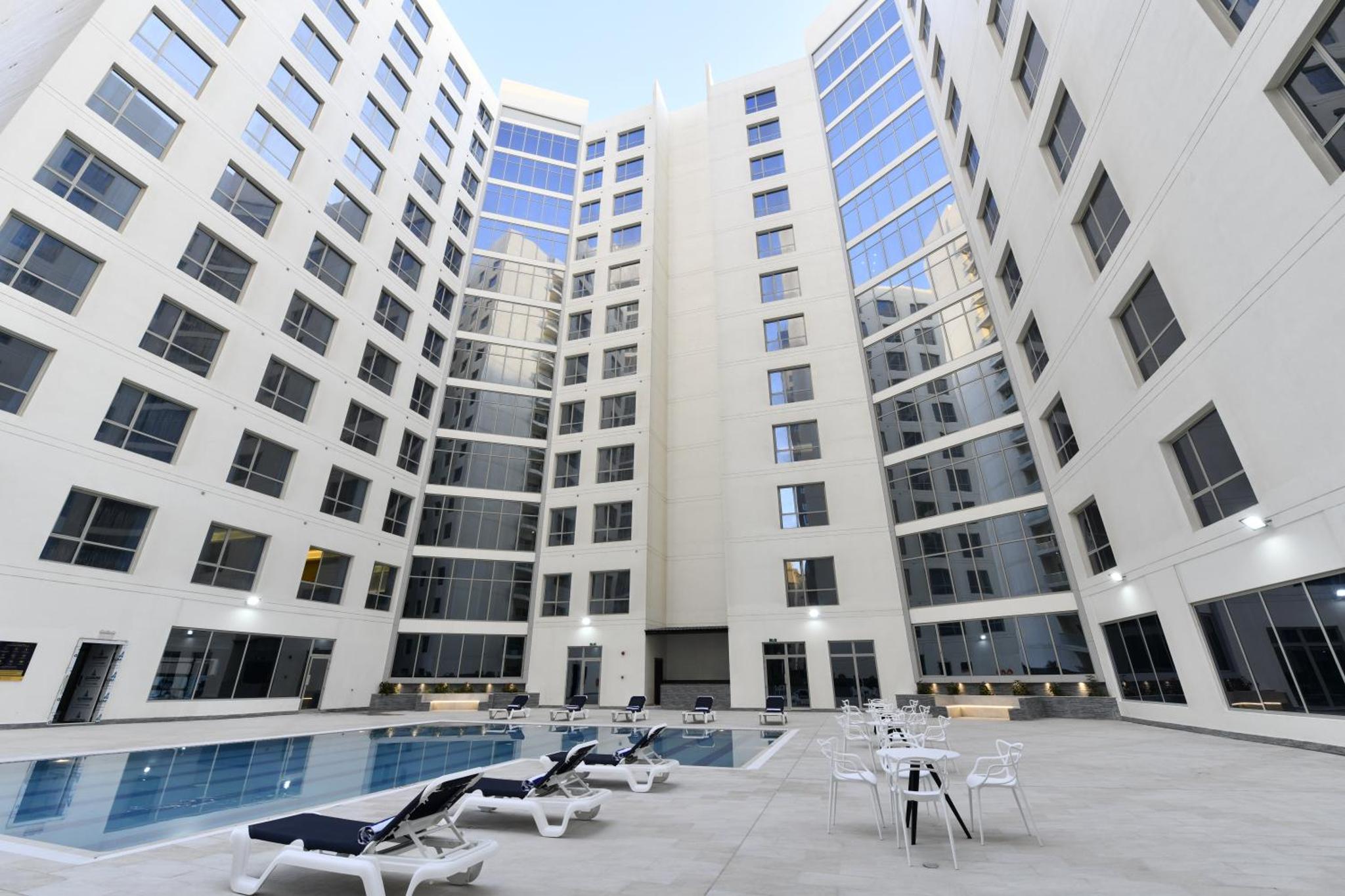 a large building with a pool and tables and chairs at JUFFAIR BOULEVARD HOTEL & SUITES in Juffair