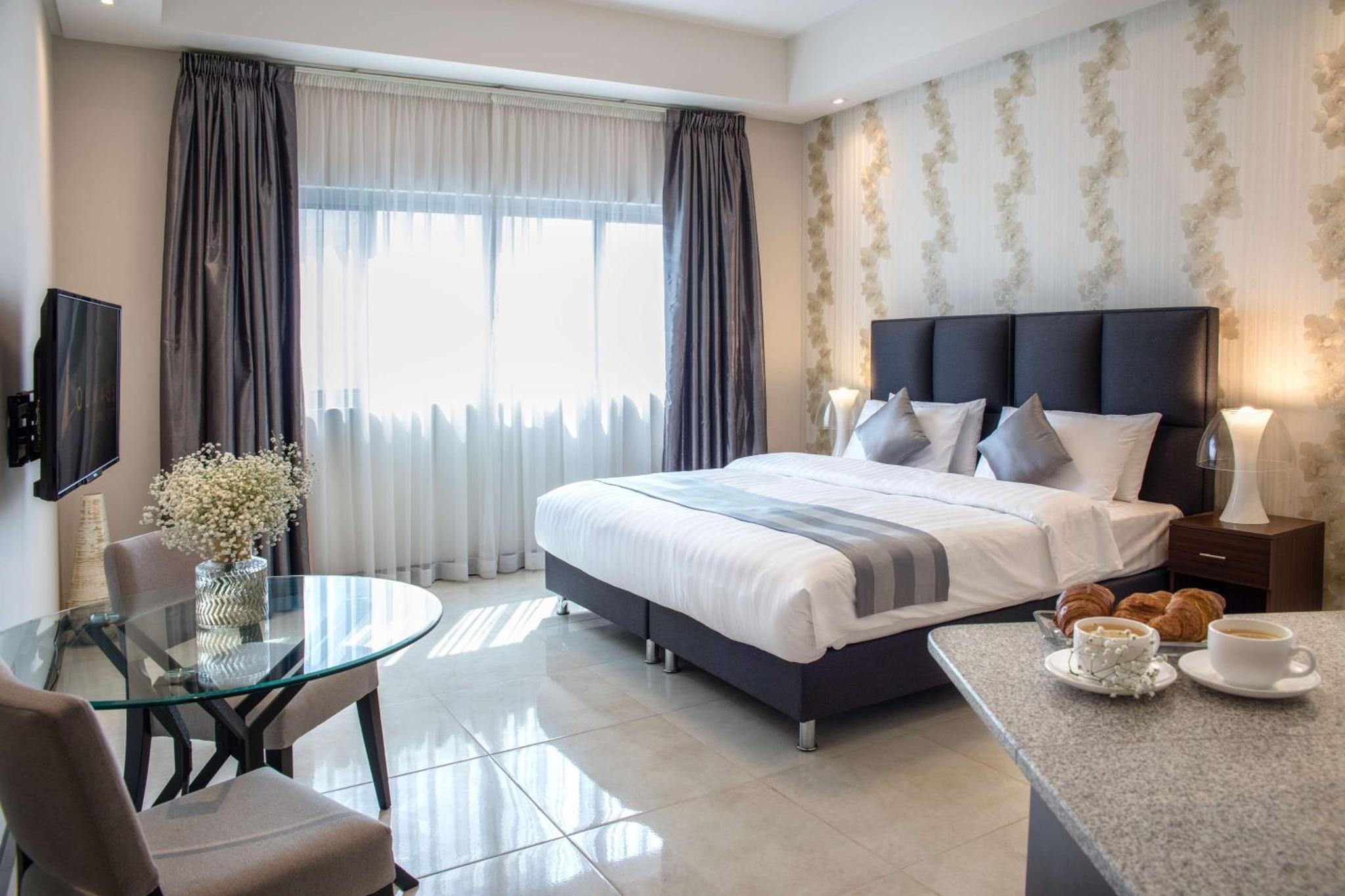 a bedroom with a large bed and a glass table at Loumage S Suites and Spa in Manama