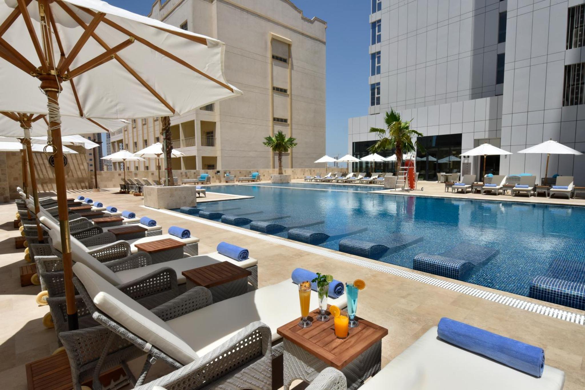 a pool at a hotel with chairs and an umbrella at Swiss-Belsuites Admiral Juffair in Manama