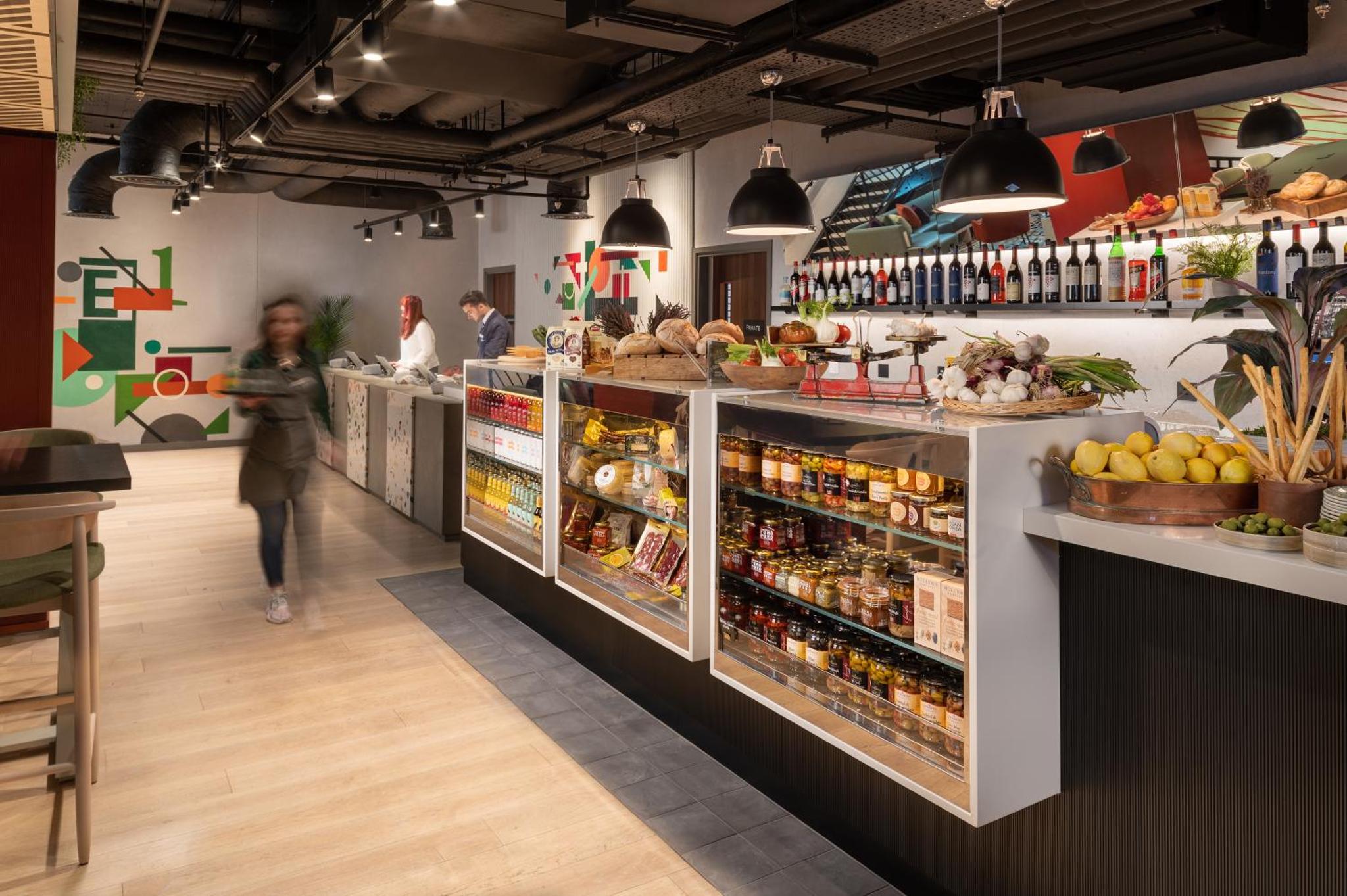 a woman walking through a grocery store with a display of food at Hyatt Place London City East in London