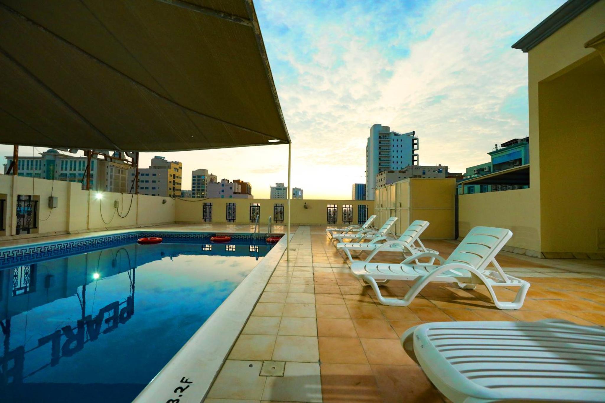 a pool with lounge chairs on a building with a city at Pearl Bahrain Suites in Manama