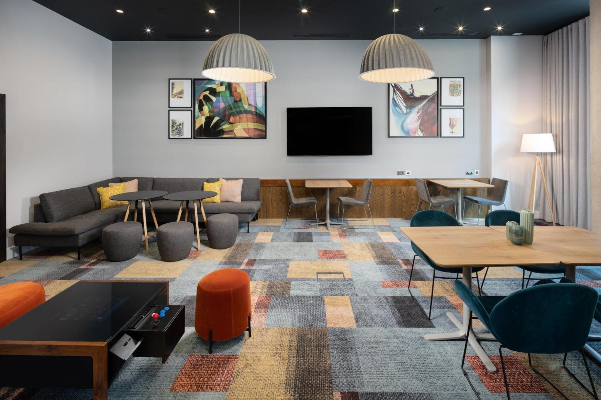 a living room with tables and chairs and a tv at Staybridge Suites London-Vauxhall by IHG in London