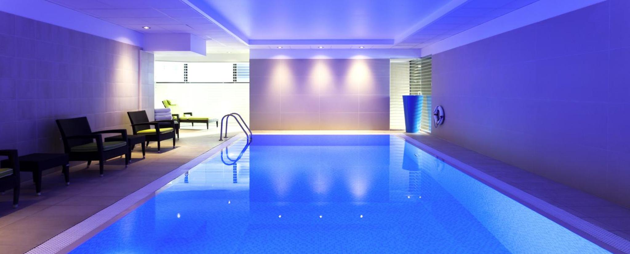 a swimming pool in a hotel with chairs and tables at Novotel London Paddington in London