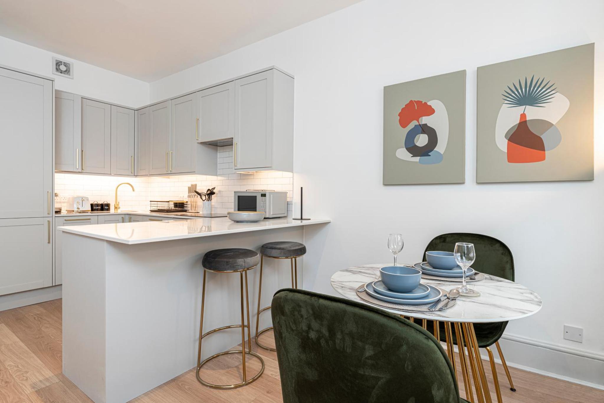 a kitchen with white cabinets and a table with chairs at Stylish 1 bed flats in Soho, next to Piccadilly Circus and Trafalgar Square in London