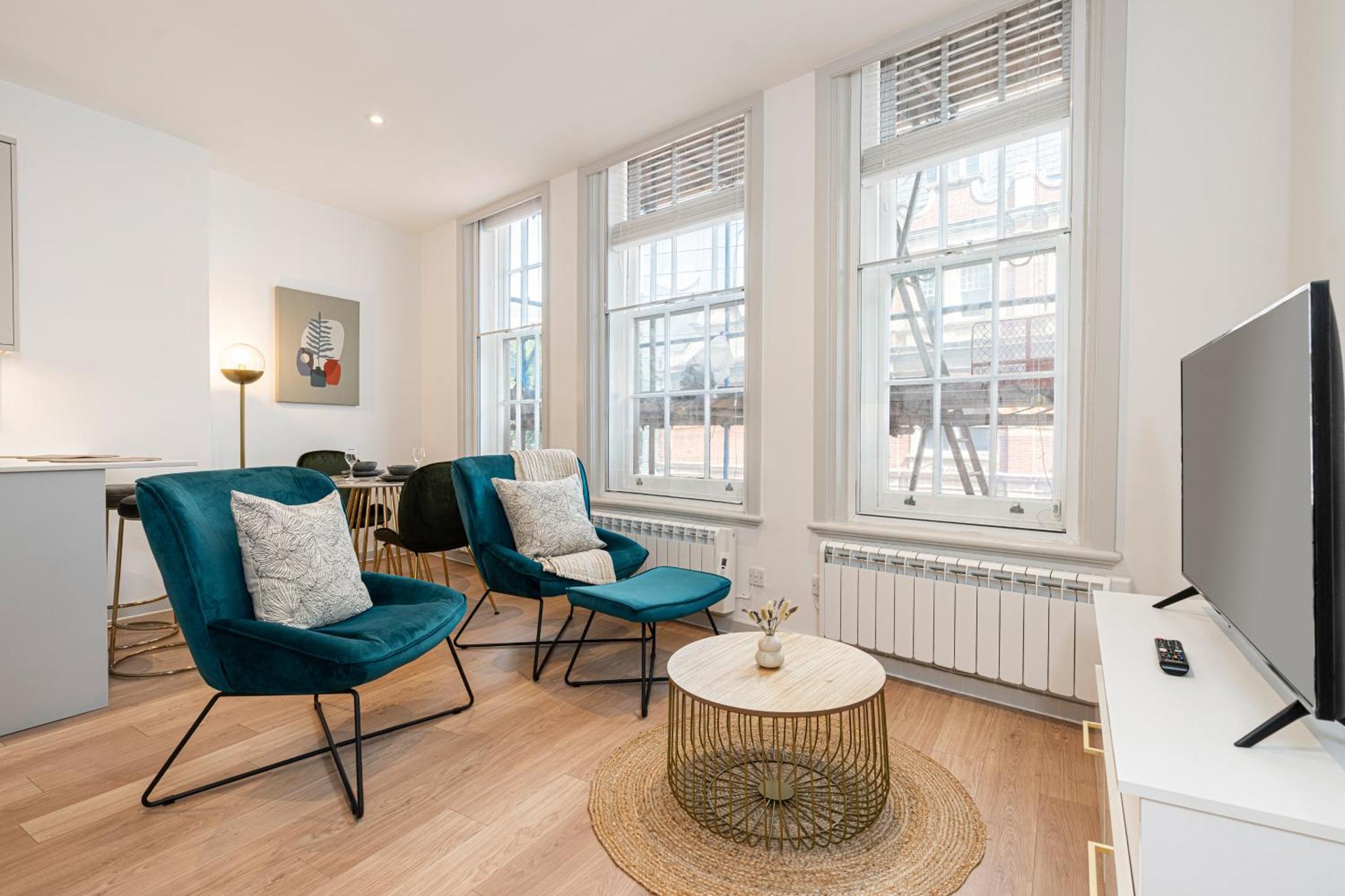 a living room with chairs and a tv and a table at Stylish 1 bed flats in Soho, next to Piccadilly Circus and Trafalgar Square in London