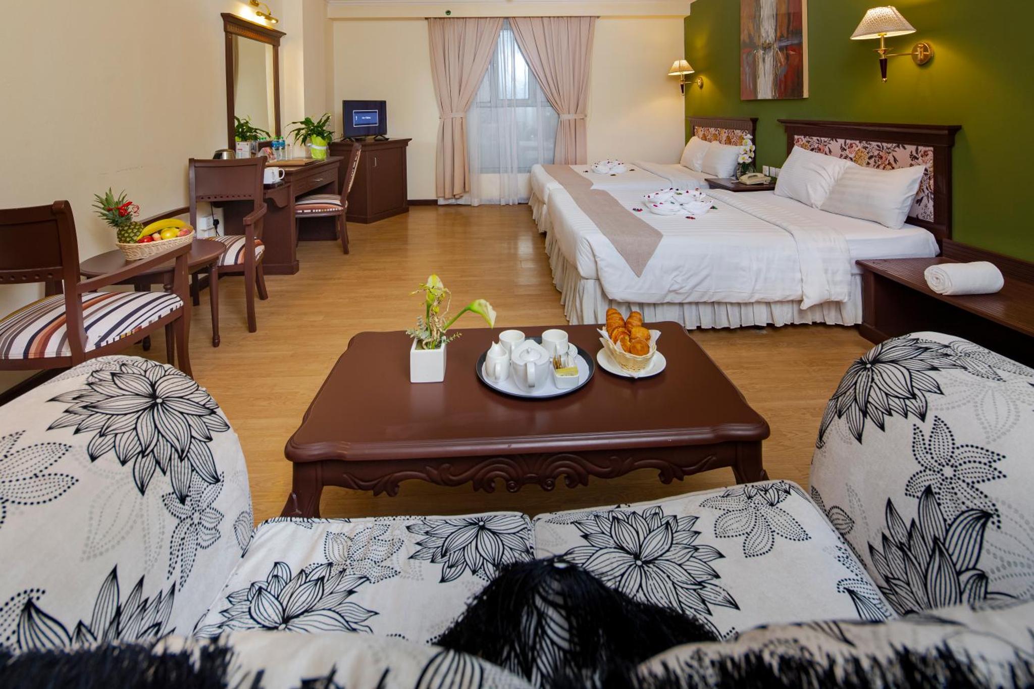 a hotel room with two beds and a table and chairs at Pars International Hotel in Manama