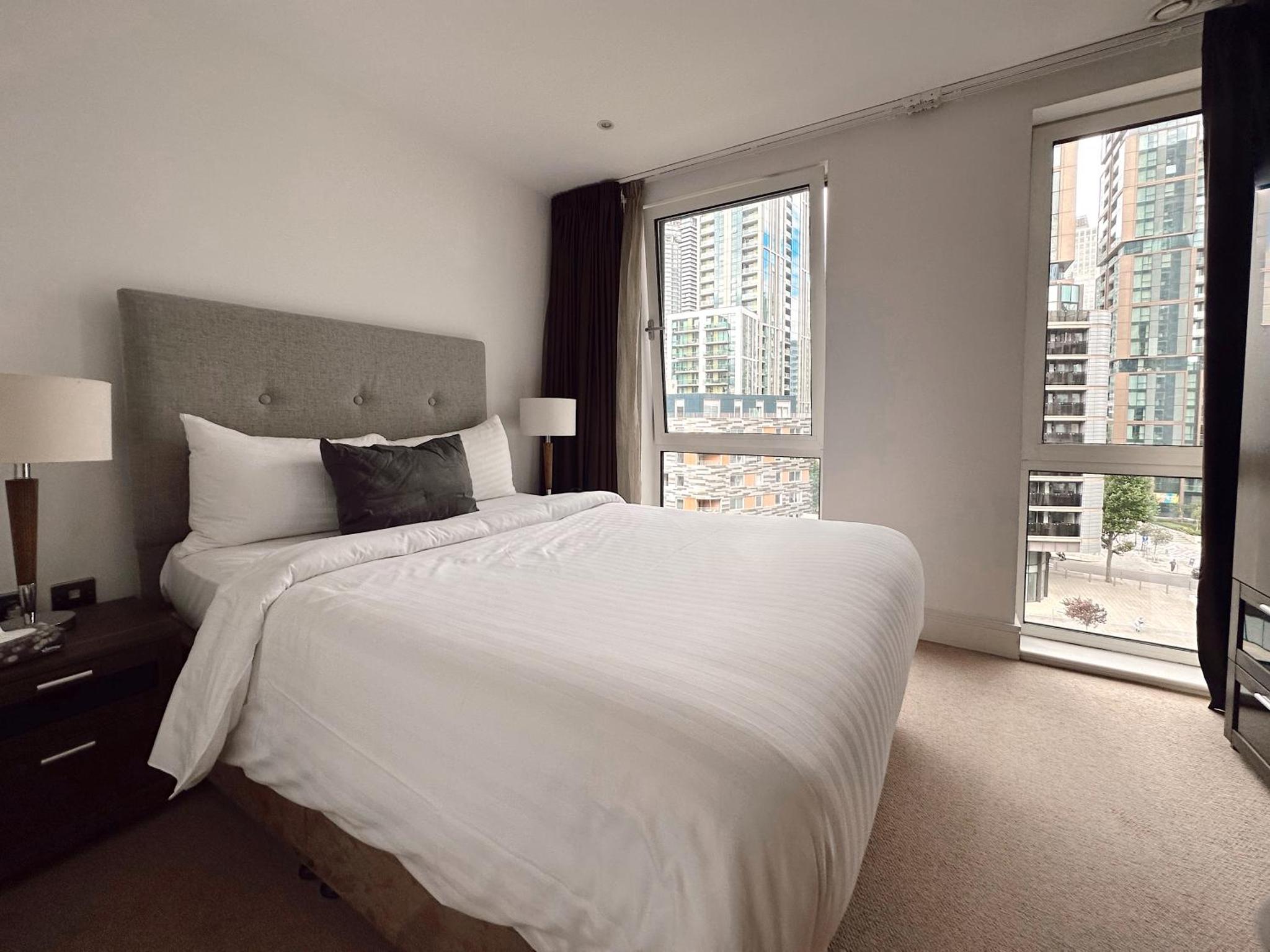 a bedroom with a large white bed and two windows at Canary Wharf - Luxury Apartments in London