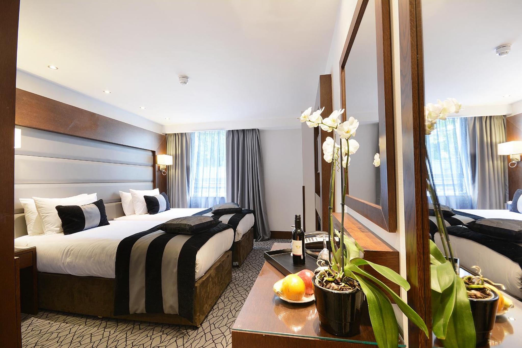 a hotel room with two beds and a mirror at Park Grand Paddington Court in London