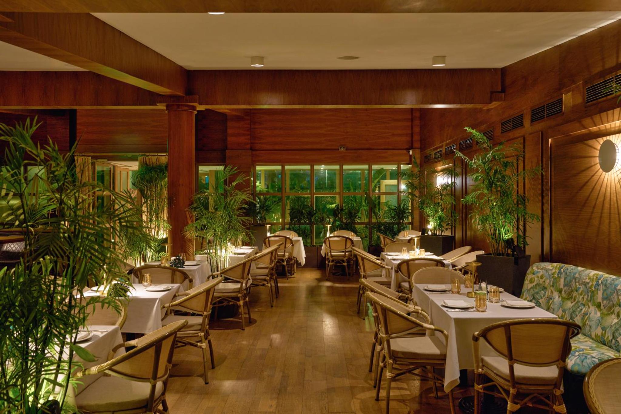 a restaurant with tables and chairs and plants at Palmyard Hotel in Manama