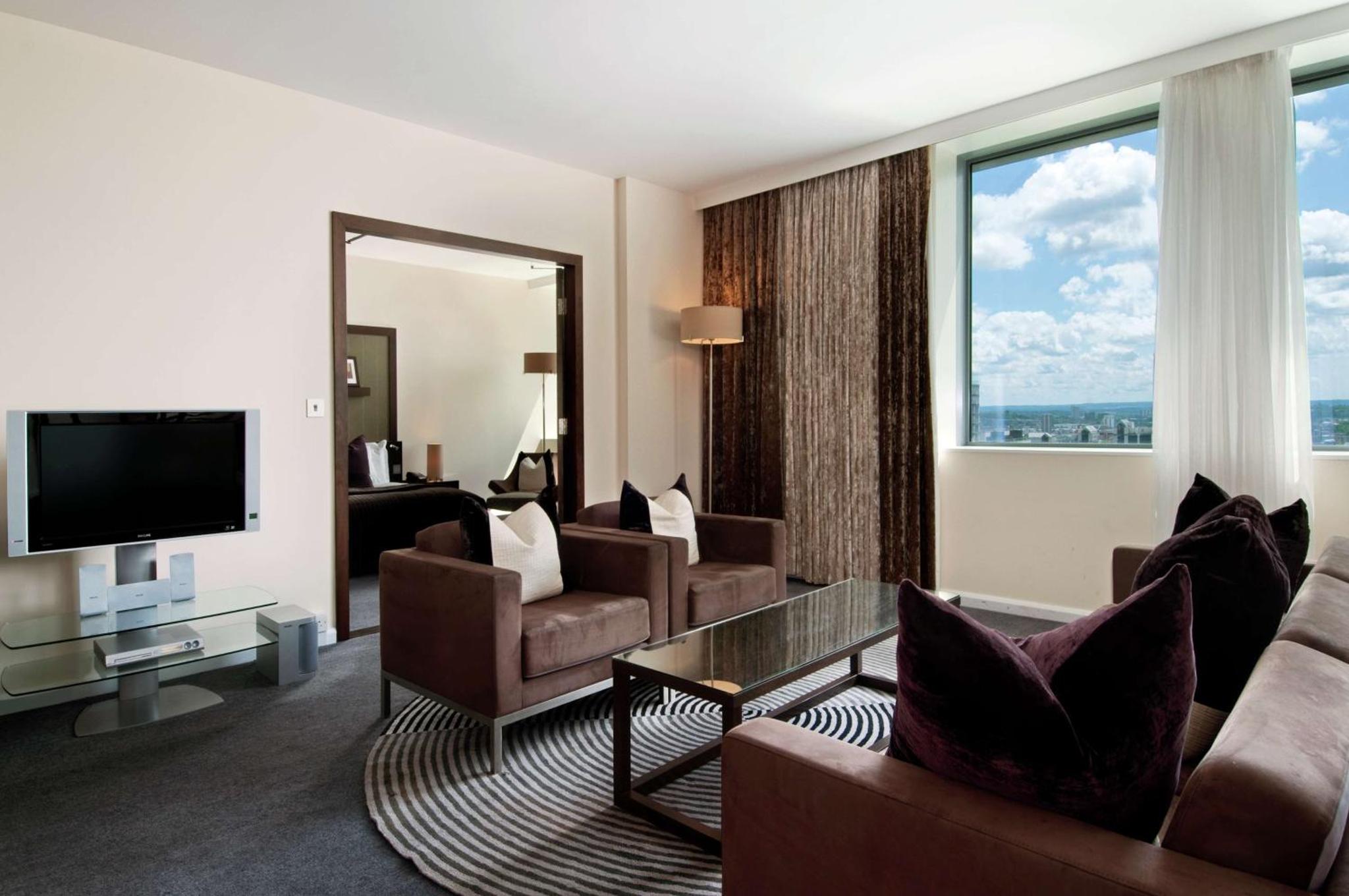 a living room with couches and a large window at Hilton London Canary Wharf in London