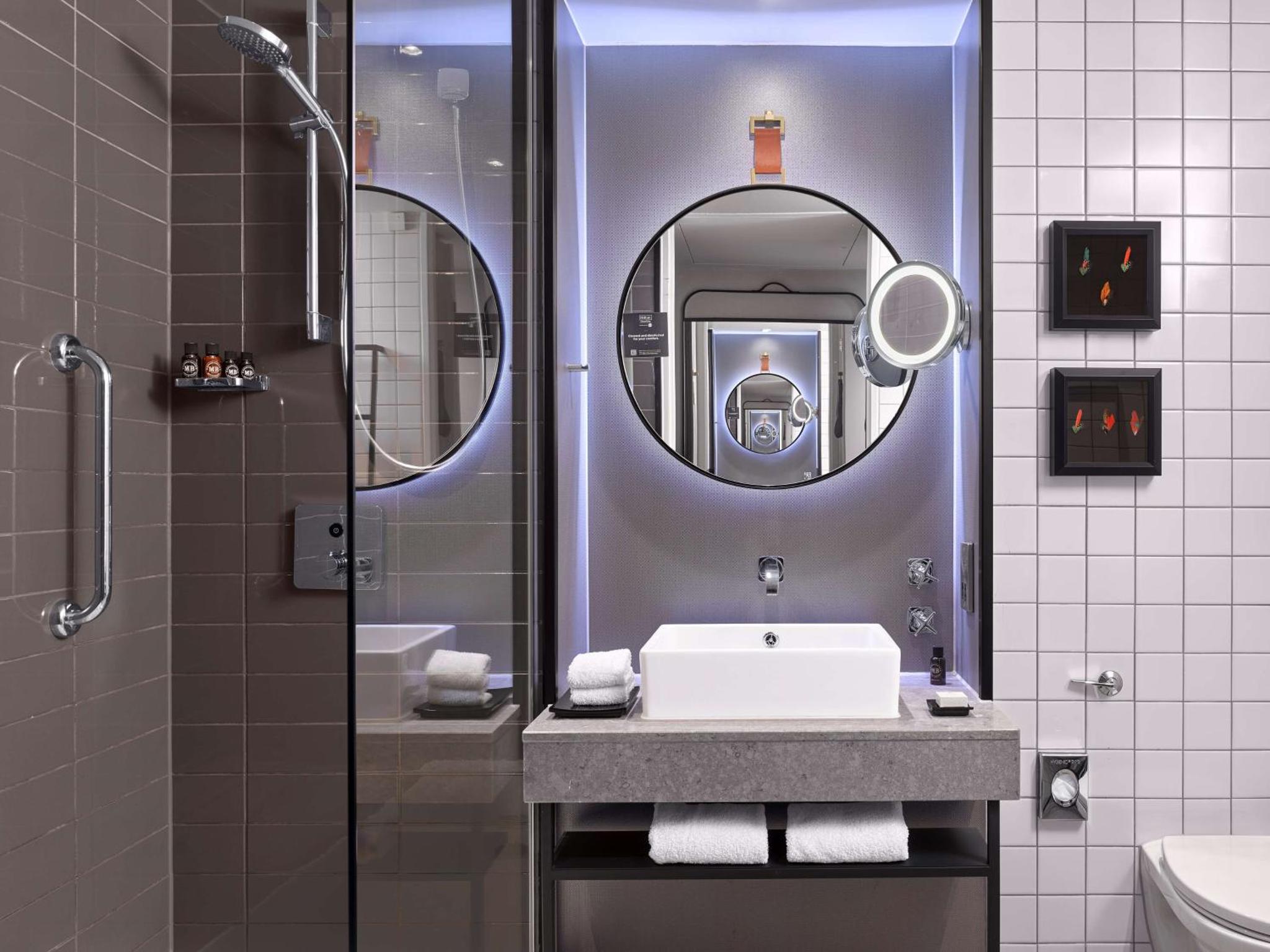 a bathroom with a sink and a shower with a mirror at The Trafalgar St James London Curio Collection by Hilton in London