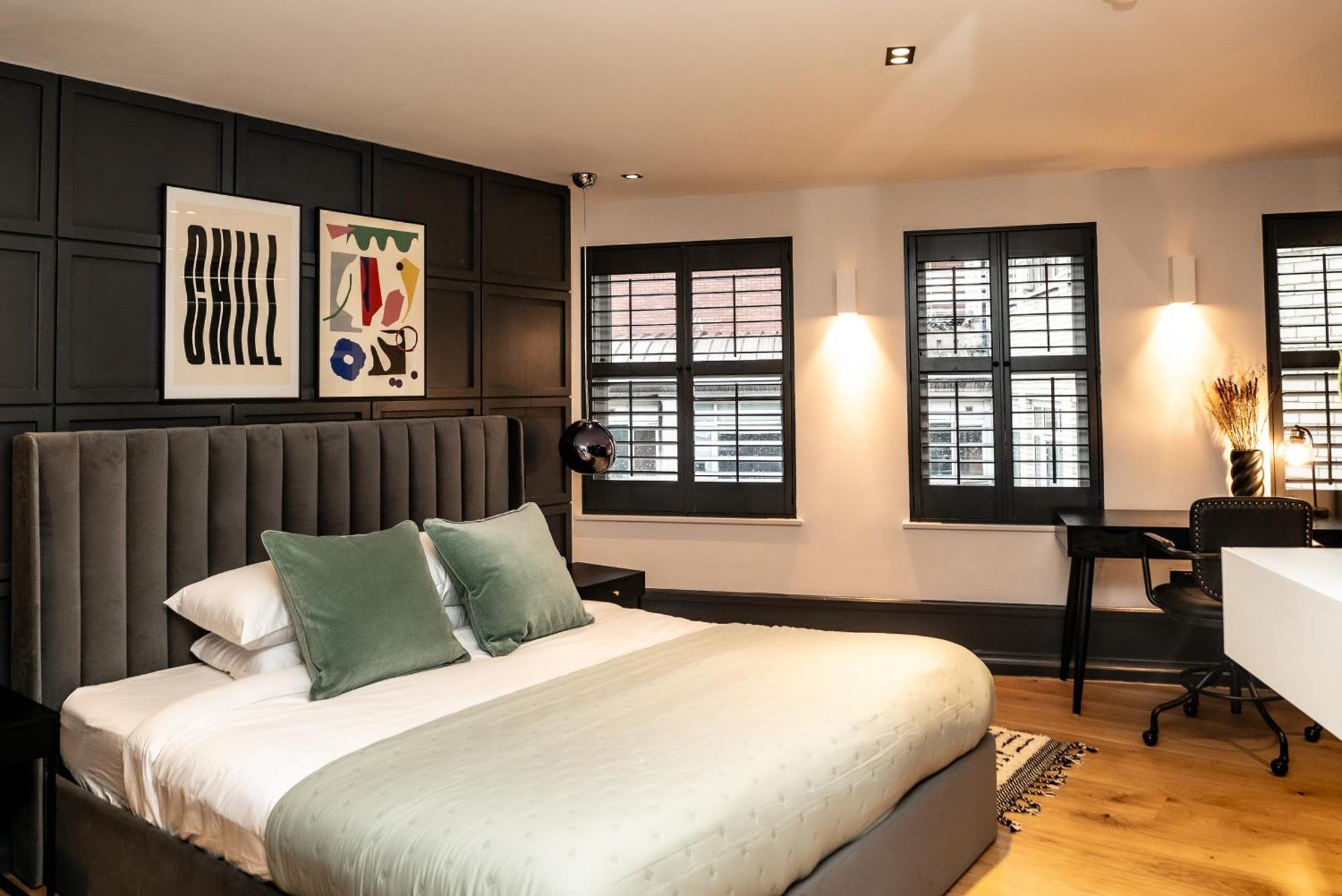 a bedroom with a bed and a desk and windows at Stay Kula London - Covent Garden Garrick St in London