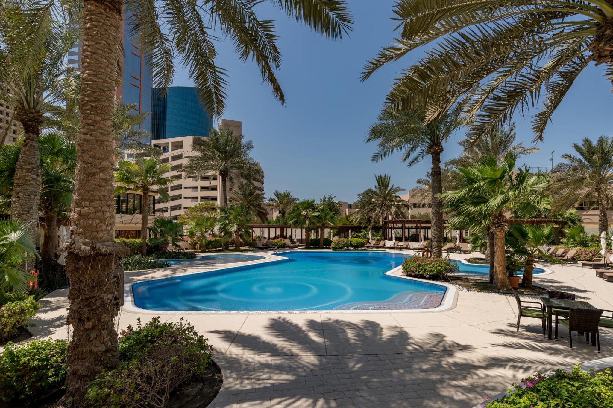 a swimming pool with palm trees in a resort at The Diplomat Radisson Blu Residence in Manama