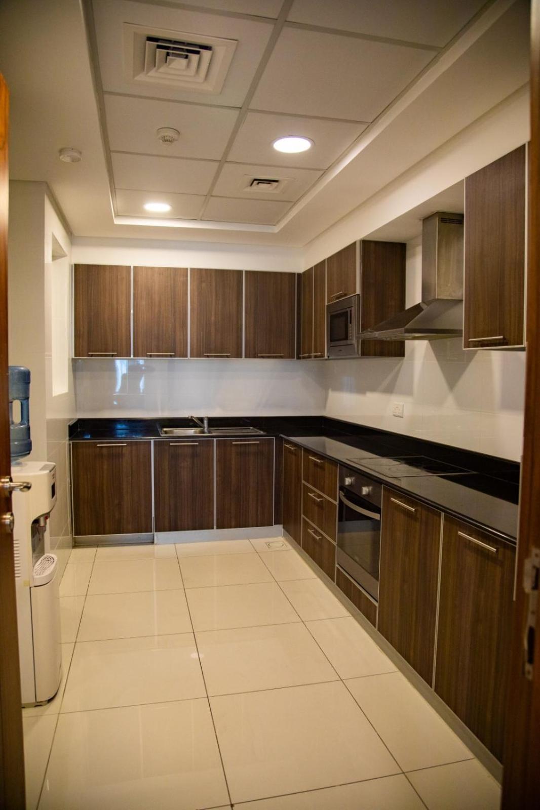 a kitchen with wooden cabinets and a white tile floor at Ginger Luxury House in Juffair