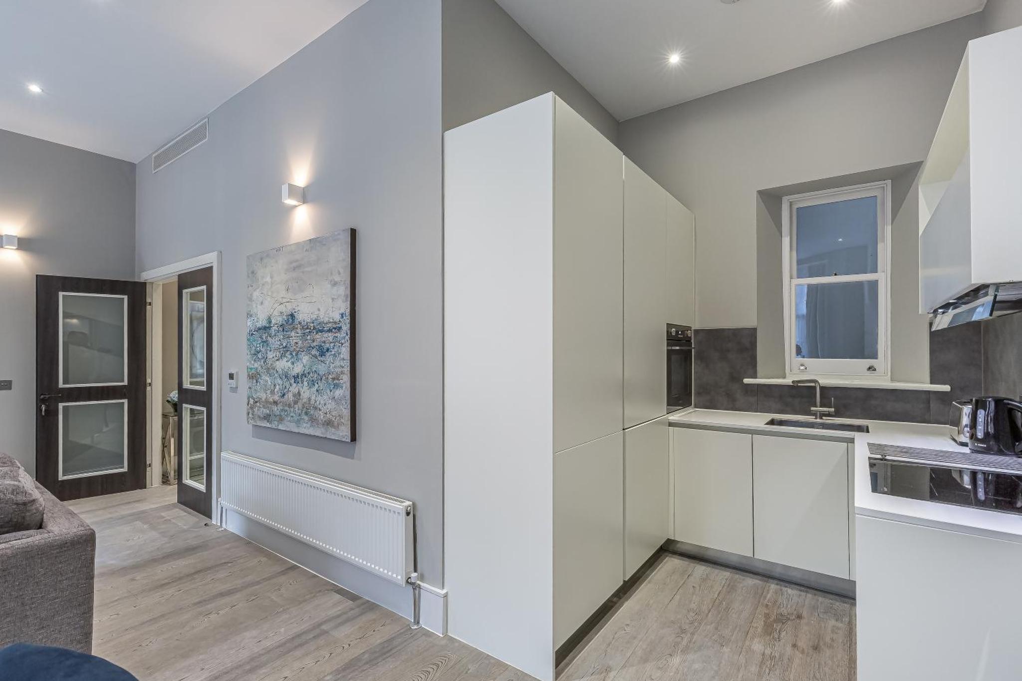 a kitchen and living room with white cabinets and a couch at Green Street Residences by Aeria Apartments in London +36 photos