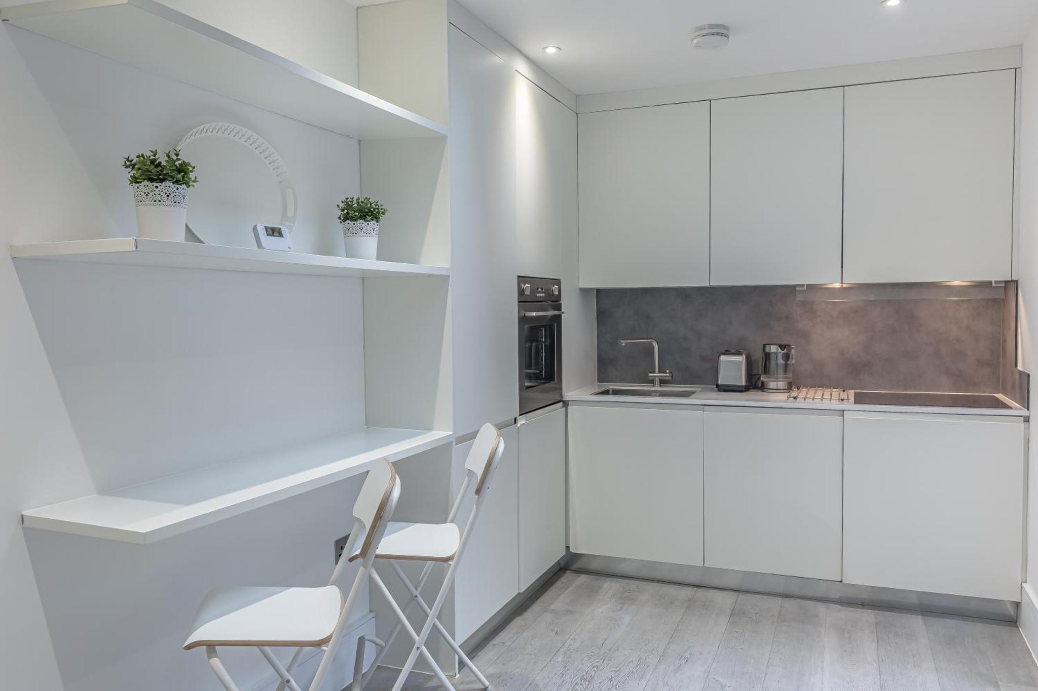 a white kitchen with white cabinets and two chairs at Green Street Residences by Aeria Apartments in London