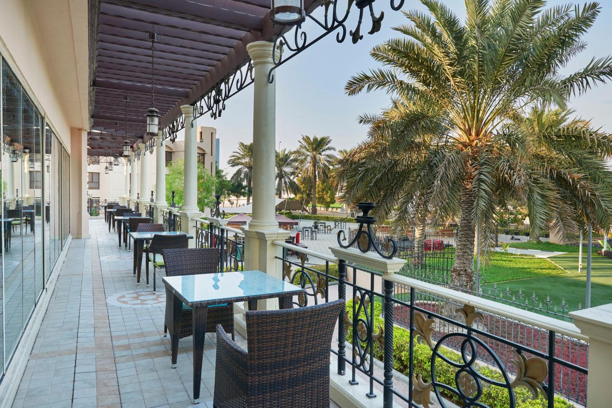 a balcony with tables and chairs and palm trees at Crowne Plaza Bahrain by IHG in Manama