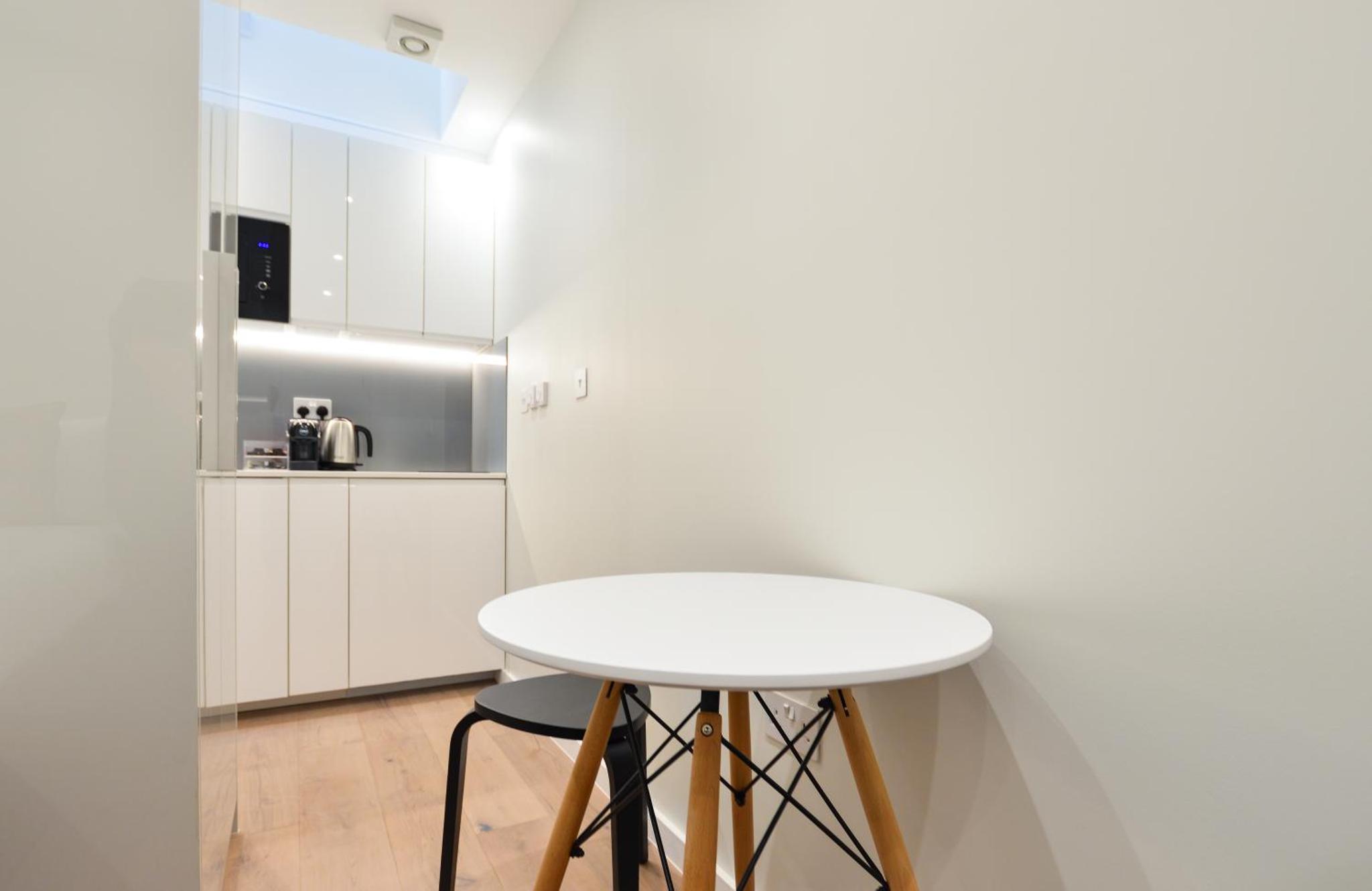 a white kitchen with a white table and stool at StayPrime Fitzrovia Serviced Apartments in London