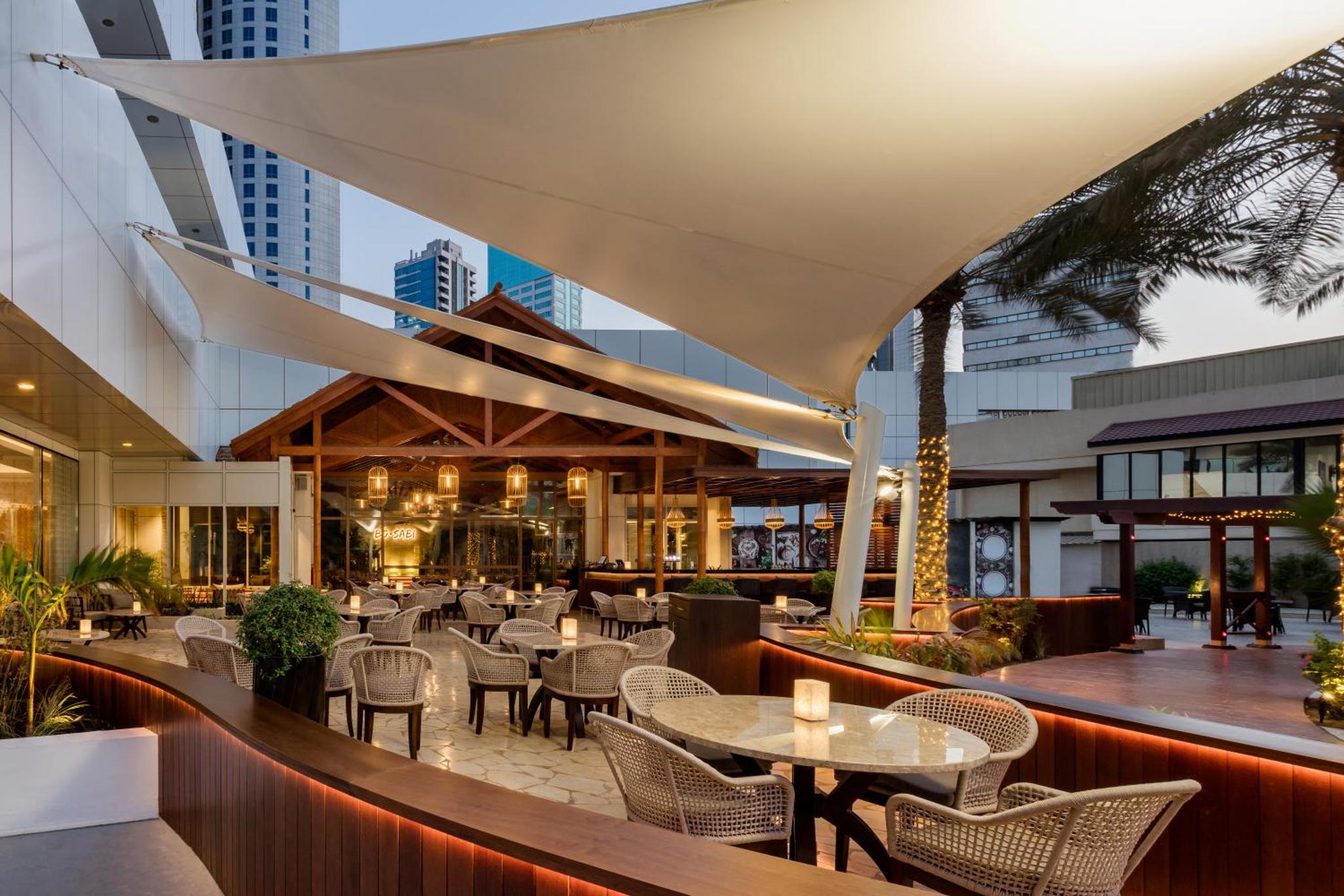 a restaurant with tables and chairs in front of a building at The Diplomat Radisson Blu Residence in Manama