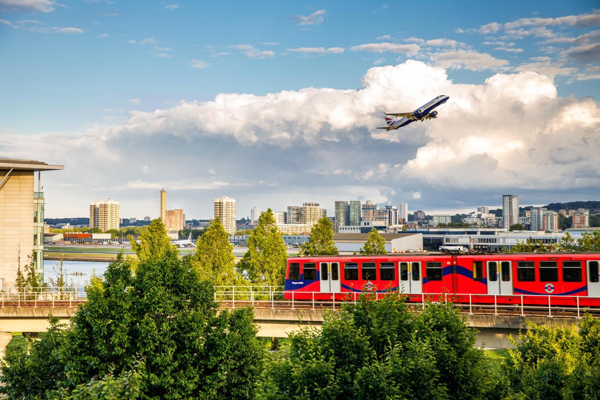 a plane is flying over a red train on a bridge at Holiday Inn Express London - ExCel by IHG in London