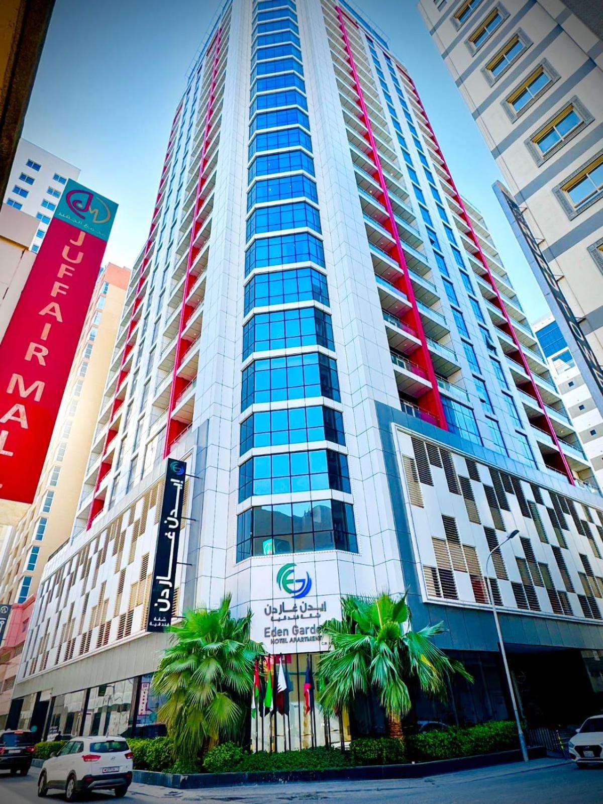 a tall building with palm trees in front of it at Eden Garden Hotel Apartment in Manama