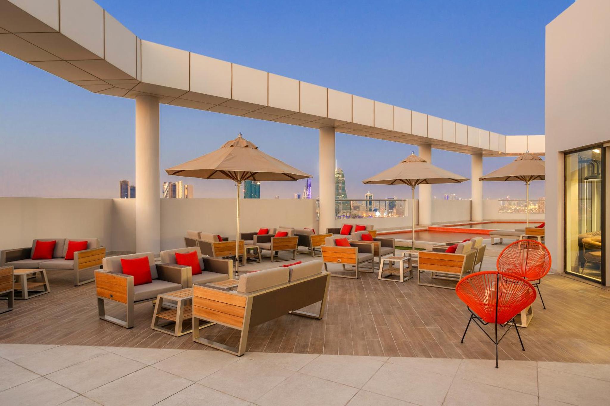 a rooftop patio with tables and chairs and umbrellas at Barcelo Hotel & Residences, Bahrain in Manama