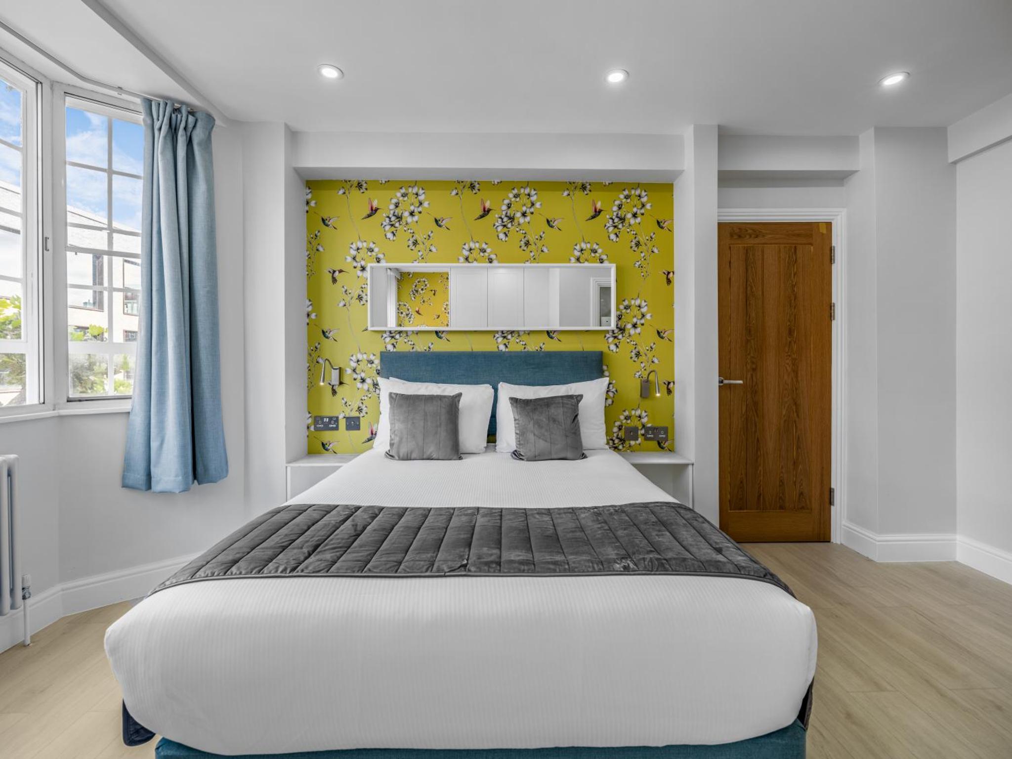 a bedroom with a large bed with a yellow wall at Chelsea Cloisters Serviced Apartments in London