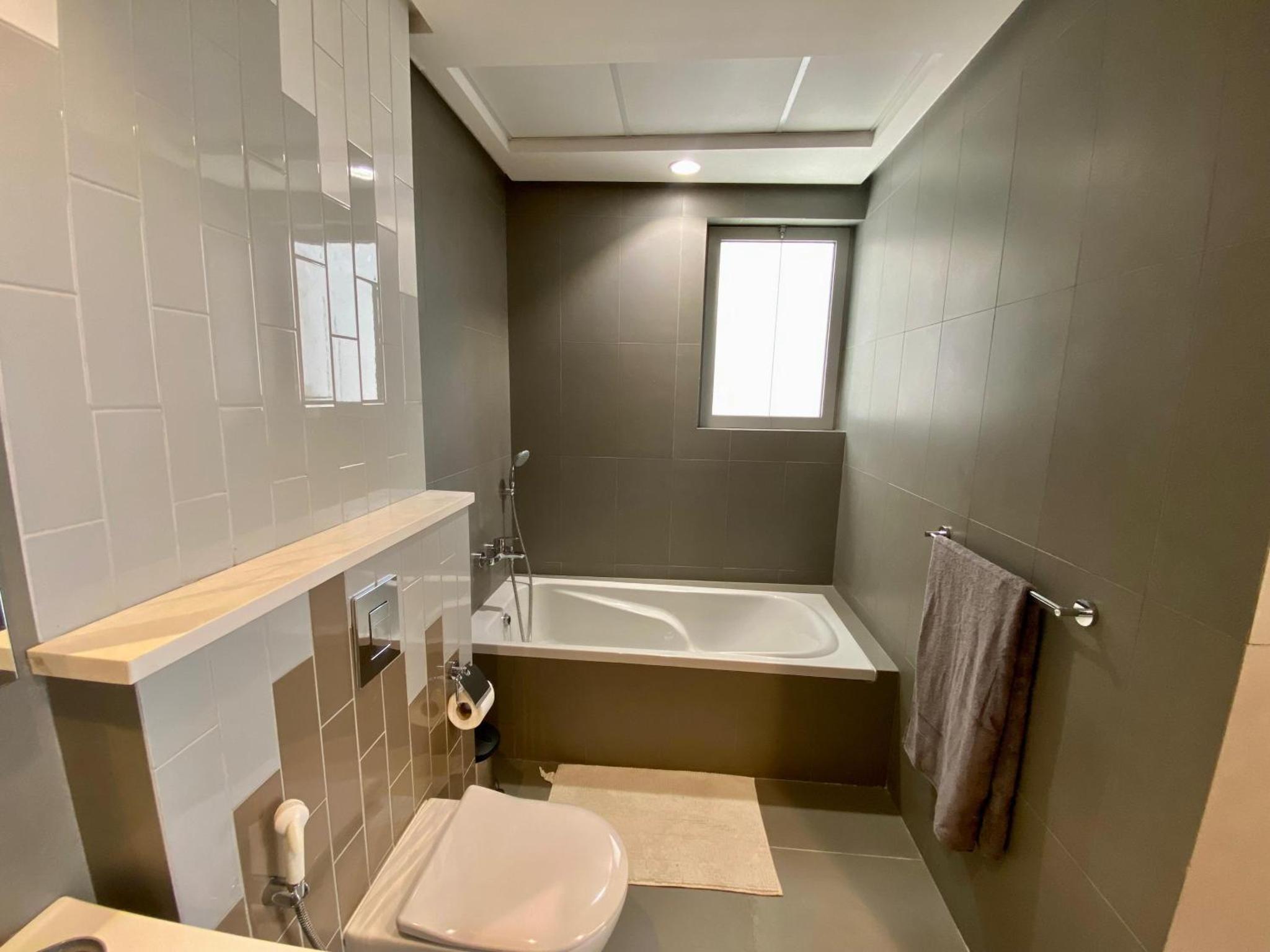 a bathroom with a tub and a toilet and a sink at Seef Serenity - Sea & City Views in Manama