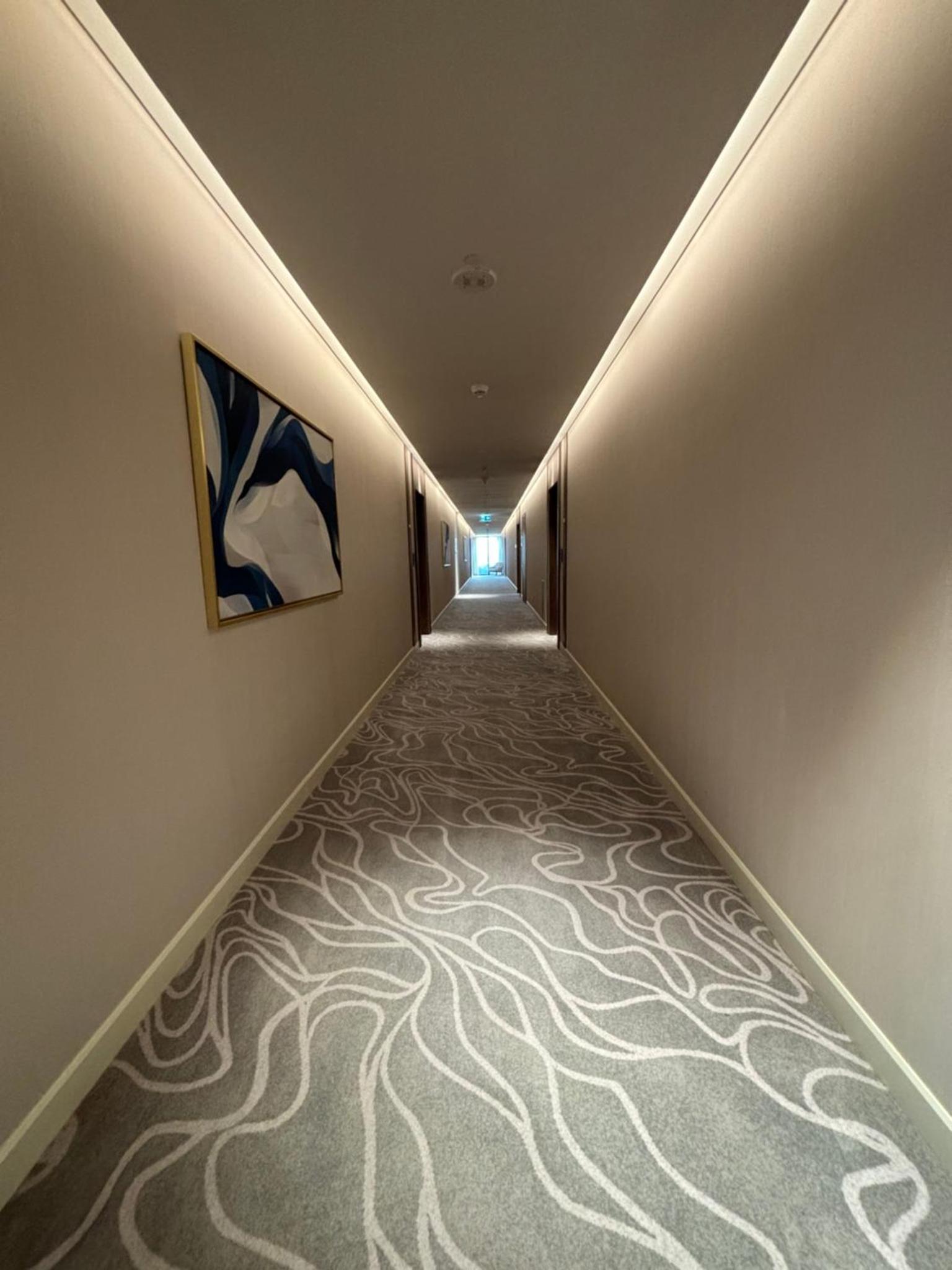a hallway with a carpeted floor with a painting on the wall at Address Beach Resort Residence - Bahrain in Rayyā